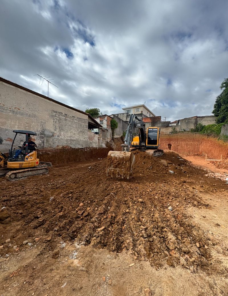 Escavadeira e trator executando terraplanagem de terreno entre casas